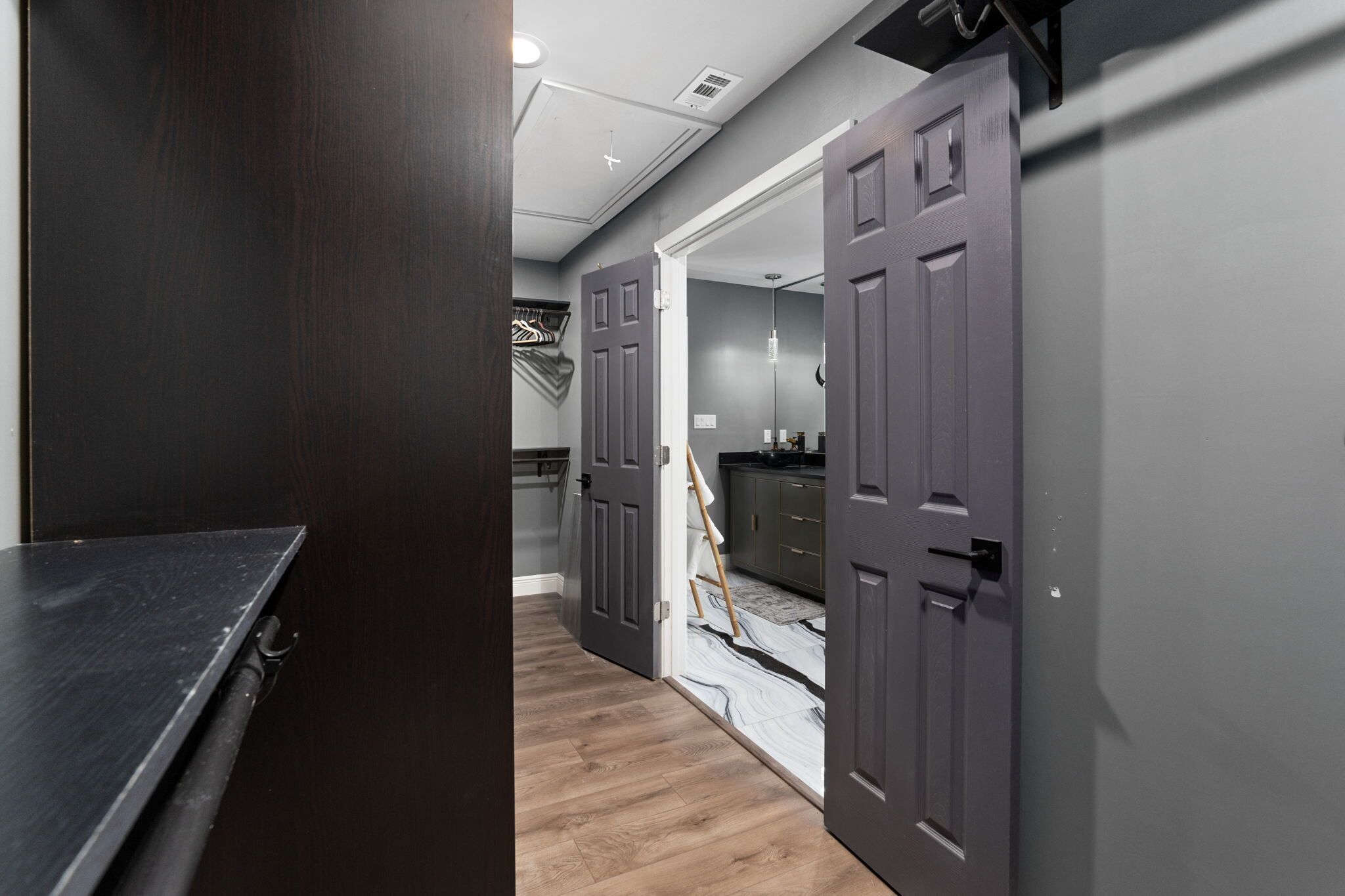 A hallway with a dark wooden bench, grey walls, and a partially open door leading to a kitchen area.