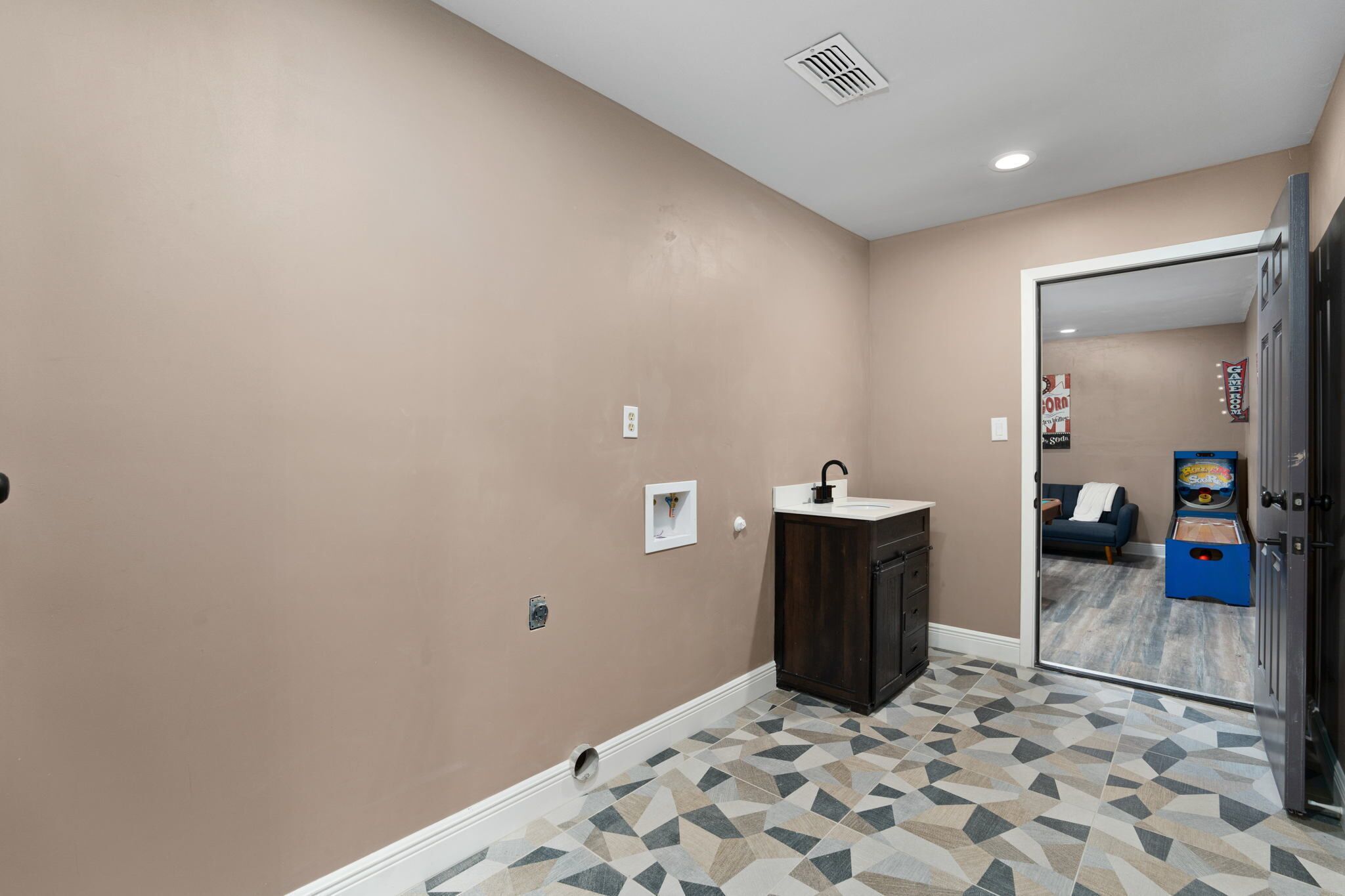 A bathroom with a beige wall, a sink, and a patterned floor.