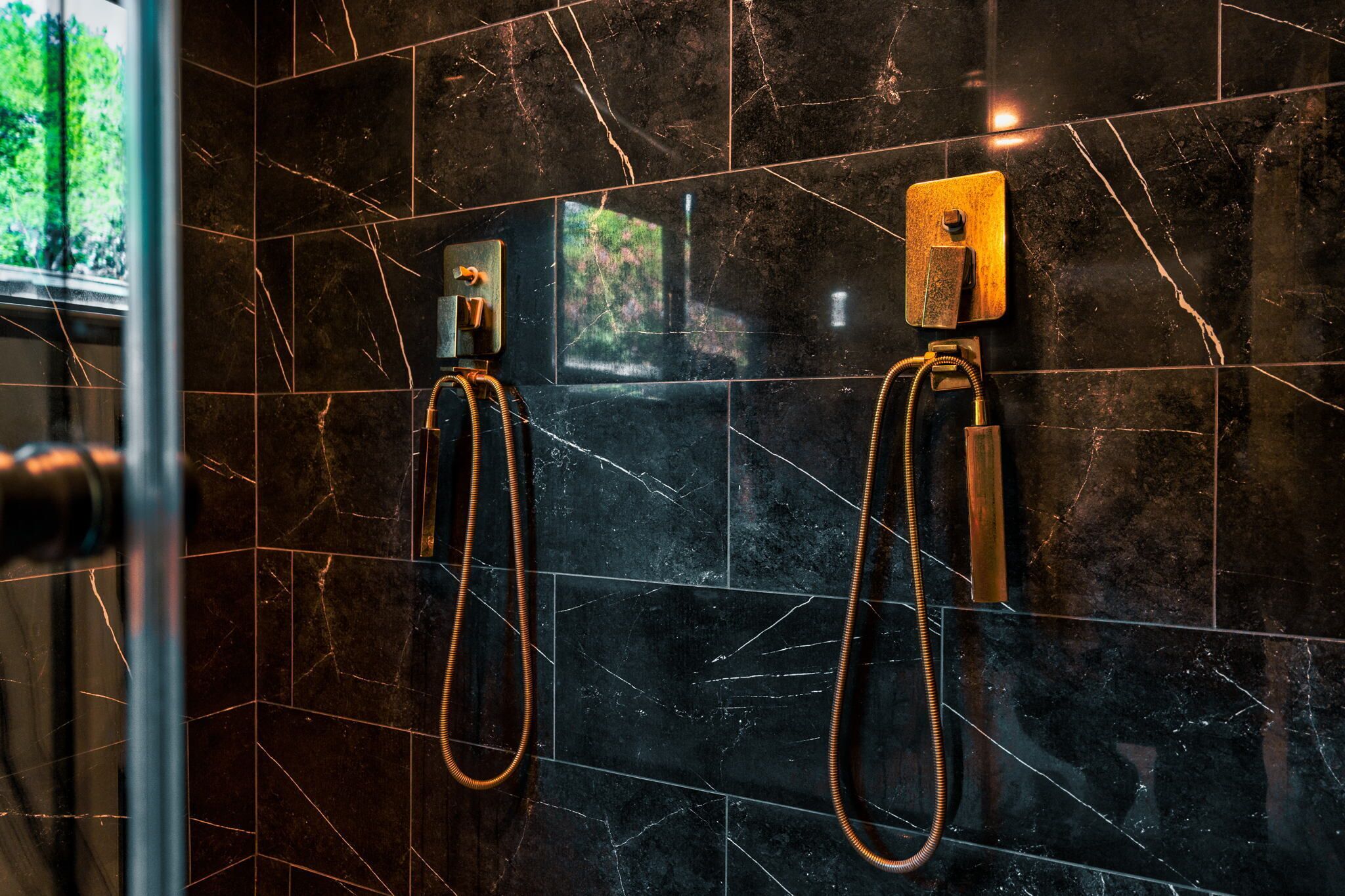 A bathroom with black marble tiles and two showerheads.