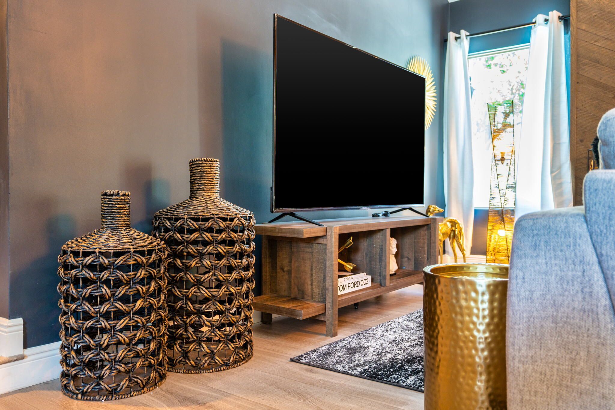 Una sala de estar moderna con un televisor de pantalla plana grande, mesas auxiliares de mimbre y un mueble de entretenimiento de madera.