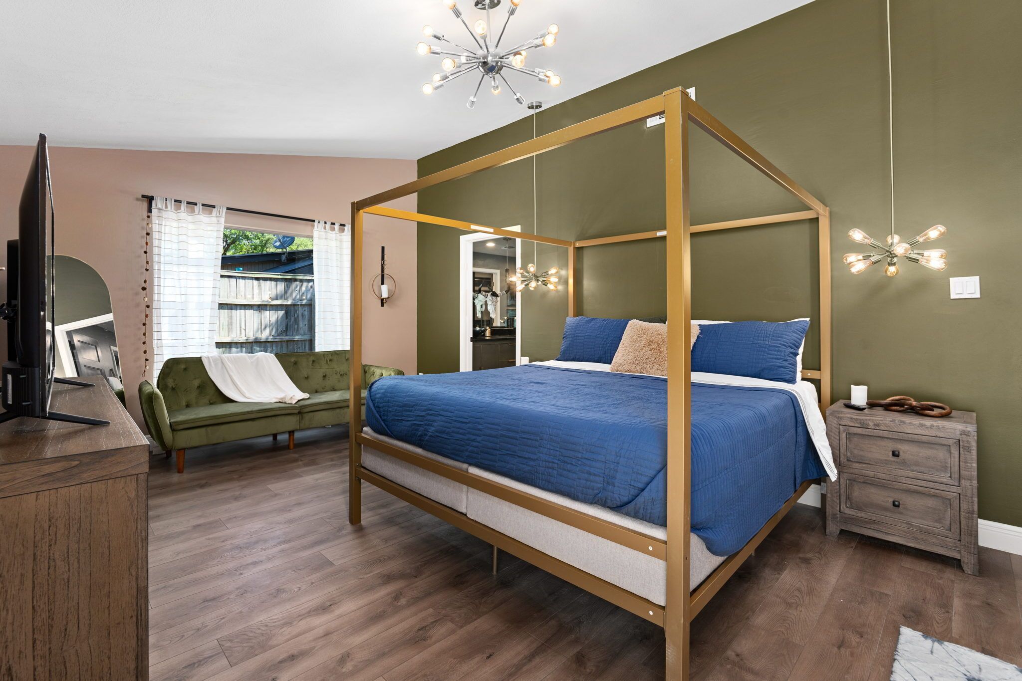Une chambre à coucher avec un lit à baldaquin, une table de chevet en bois, un canapé vert et un téléviseur posé sur un bureau en bois.