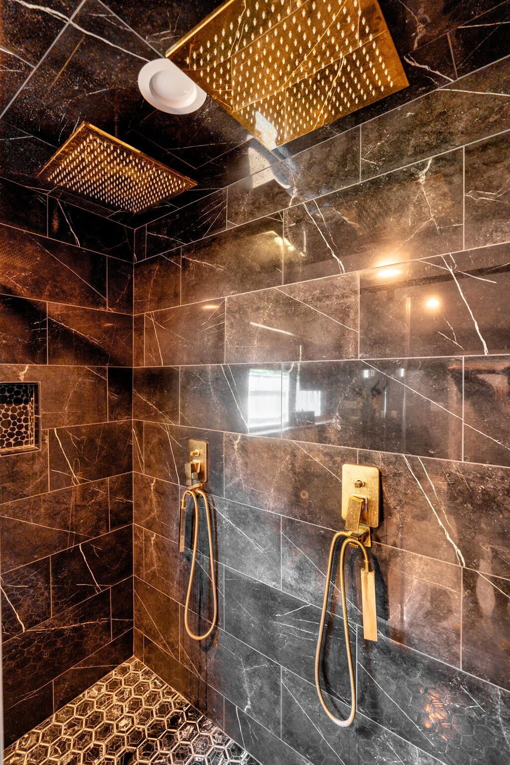 A modern bathroom with dark marble tiles, a geometric shower design, and two gold fixtures.