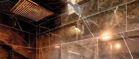 A modern bathroom with dark marble tiles, a geometric shower design, and two gold fixtures.