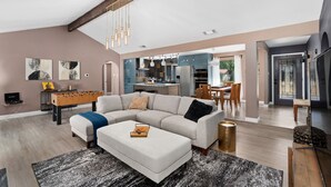 A spacious living room with a large sectional sofa, a foosball table, and a modern kitchen in the background. - Sinatra Fun 5BD Home Huge Pool Game Room (Round Rock)