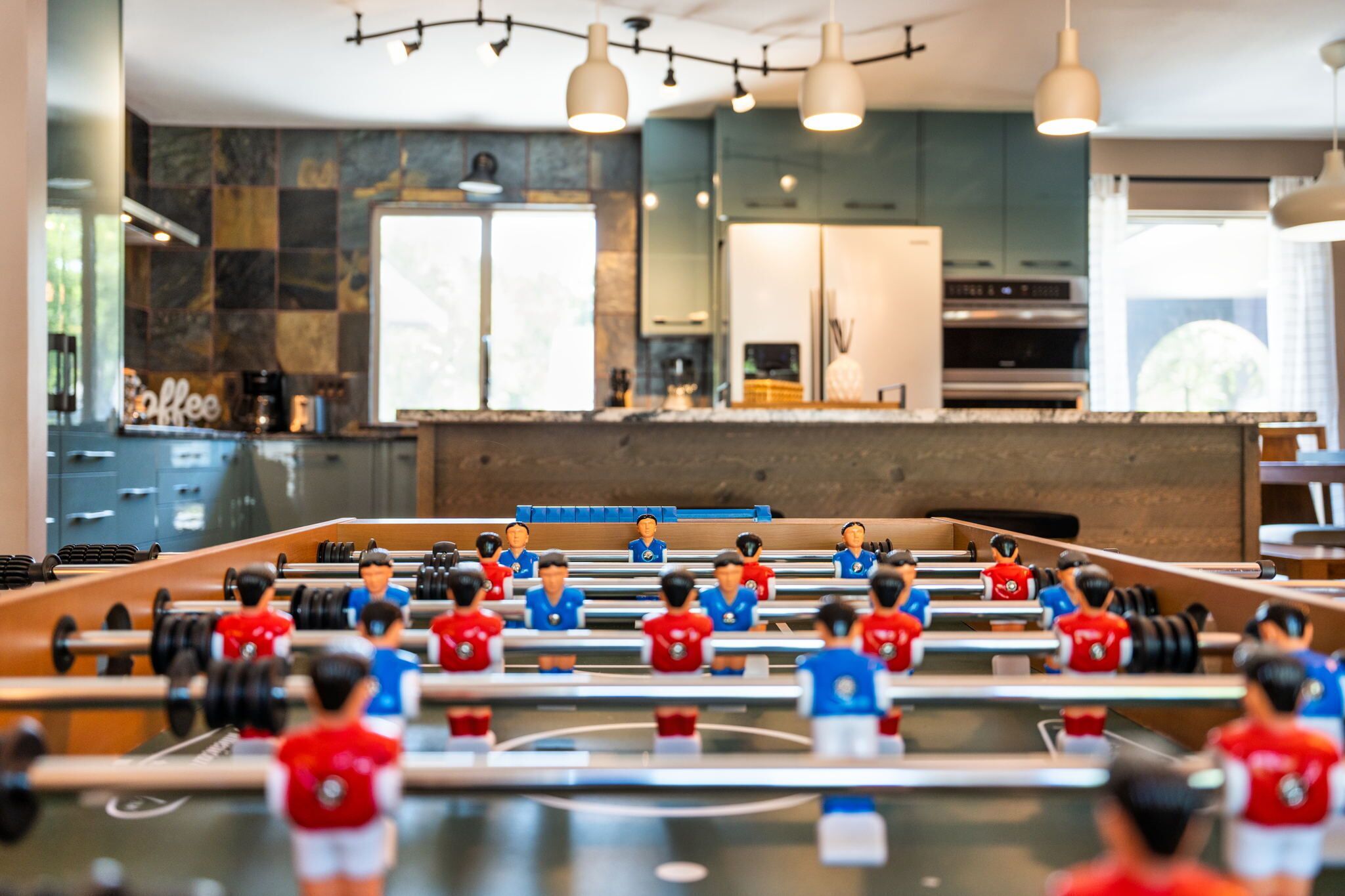 A foosball table in a modern kitchen with marble backsplash and pendant lighting.