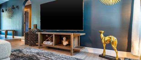 A modern living room with a large flat-screen TV on a wooden stand, a decorative golden statue, and a patterned rug.