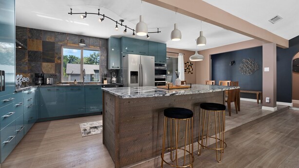 A modern kitchen with a large island, bar stools, and a view of the outdoors. - Sinatra Fun 5BD Home Huge Pool Game Room (Round Rock)