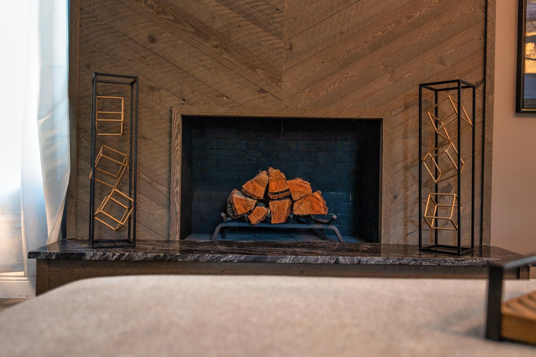 A fireplace with a log fire, wooden beams on the ceiling, and two geometric metal stands on either side.
