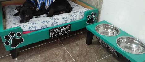 A pet bed with a blue and white pattern, a metal feeding station, and a tiled floor.
