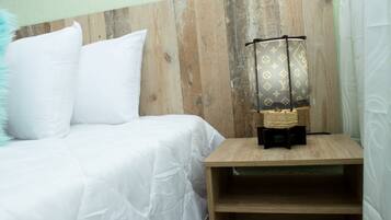 Cabecera de madera, una cama con ropa de cama blanca y una mesita de noche con una lámpara.