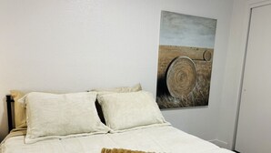 Un lit bien fait, avec une couette blanche et deux oreillers, un plaid marron et un tableau représentant un tonneau en bois accroché au mur.