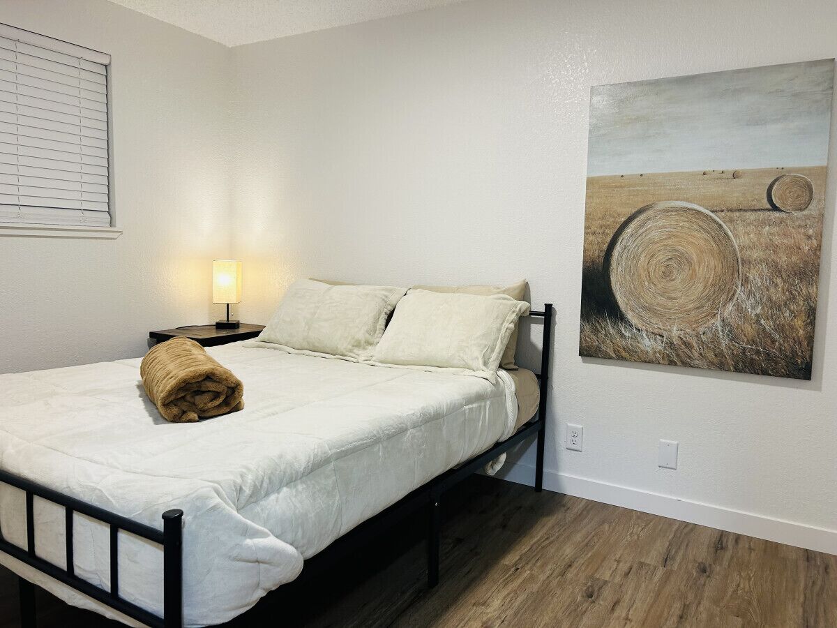 Une chambre à coucher avec un lit, une lampe de chevet, une serviette enroulée et un tableau accroché au mur.