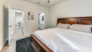 A bedroom with a large bed, a ceiling fan, and a hallway leading to a bathroom.