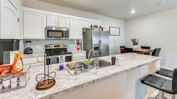 A modern kitchen with white cabinets, stainless steel appliances, and a marble countertop.
