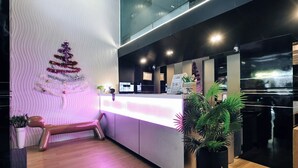 A reception area with a modern design, featuring a reception desk, a bench, and a decorative Christmas tree. - Deco Lux Hotel (Bangkok)