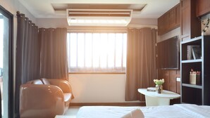 A hotel room with a bed, a sofa, a small table with a vase, and a bookshelf. - Deco Lux Hotel (Bangkok)
