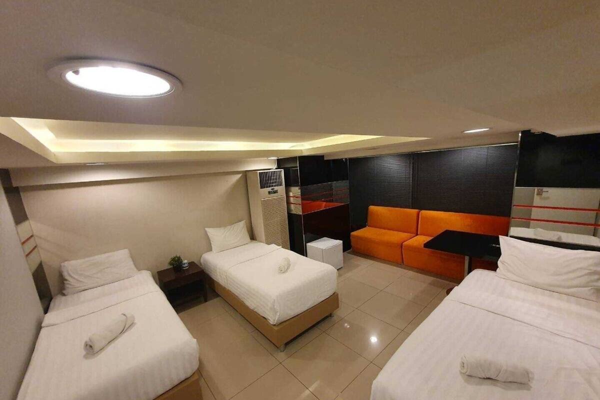 A hotel room with three beds, a sofa, a small table, and a ceiling light.