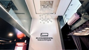 A hotel interior with a modern chandelier, a sign with the hotel's name, and a visible air conditioning unit. - Deco Lux Hotel (Bangkok)