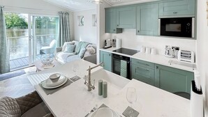 Una cucina moderna con isola centrale, un'area pranzo con tavolo apparecchiato per due e vista su un fiume tramite una porta scorrevole in vetro.