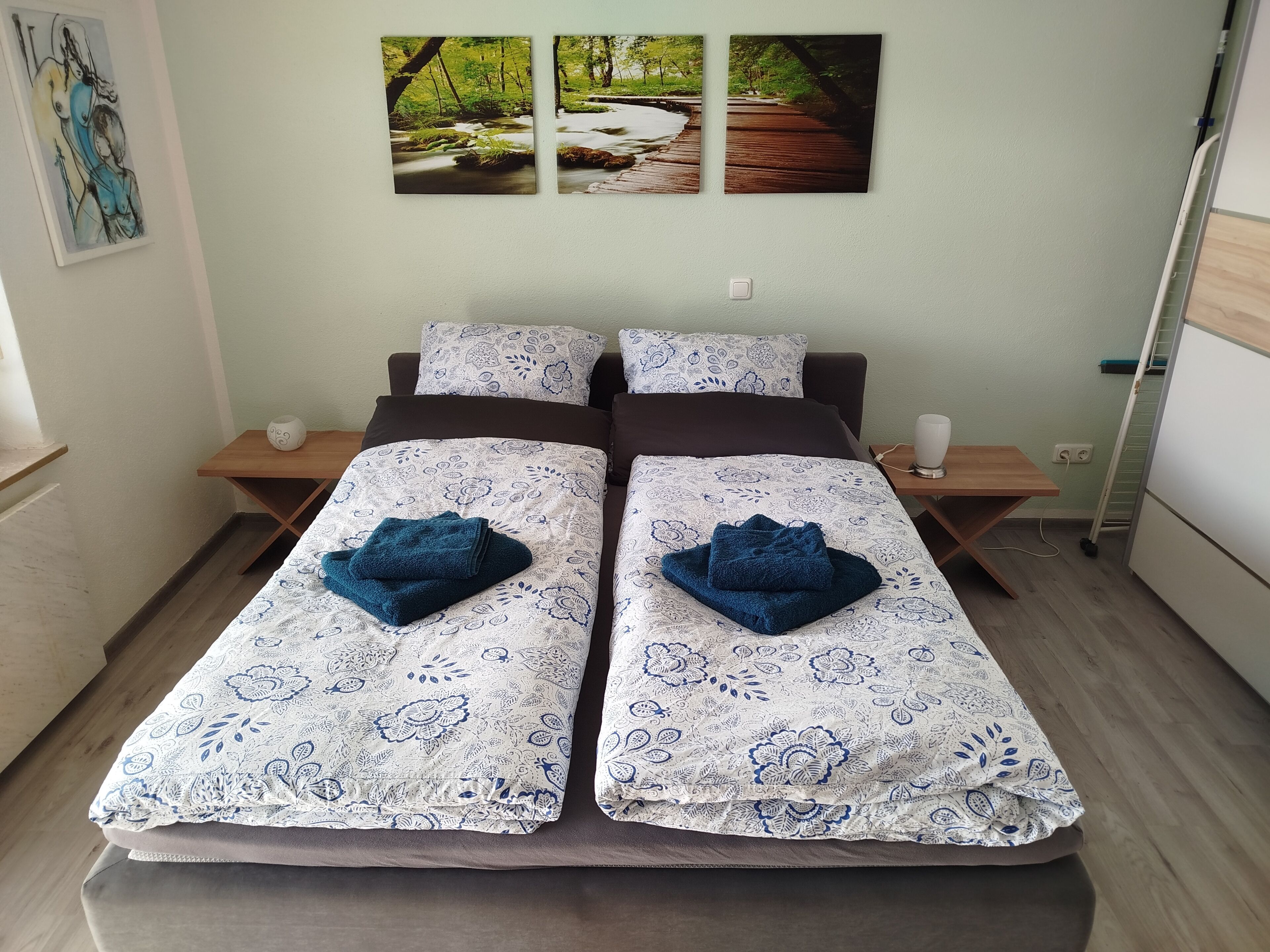 A double bed with floral-patterned bedding, two bedside tables, and a wall-mounted artwork.