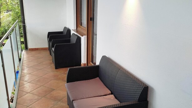 Ein Balkon mit Rattanmöbeln, einer Holzdecke und einem Fenster mit Blick auf Grünflächen.