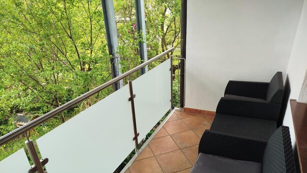 Un balcon doté d’une rambarde en métal, d’un sol carrelé et d’un espace salon avec des meubles en rotin foncé.