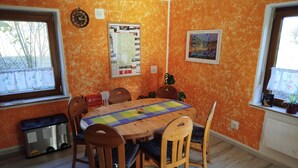 Un coin repas avec une table en bois, des chaises, une courtepointe et un tableau d’affichage sur des murs de couleur orange.