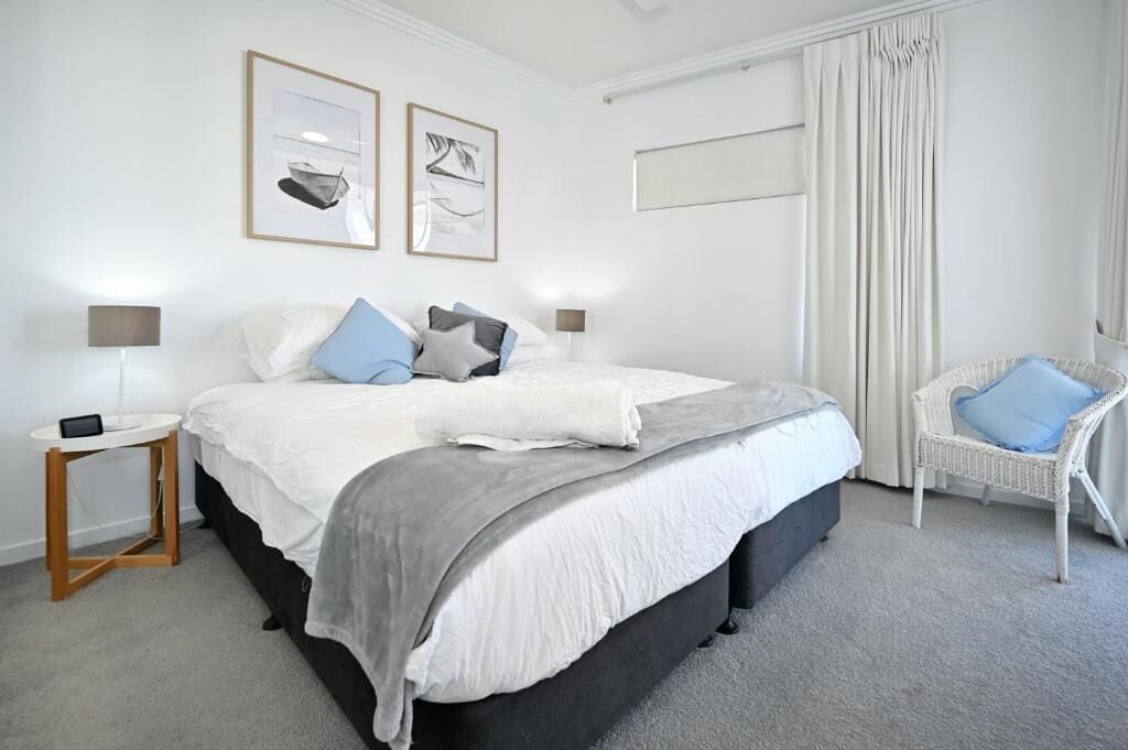 Une chambre à coucher moderne avec un grand lit, deux tables de chevet, une chaise et des œuvres d’art accrochées au mur.