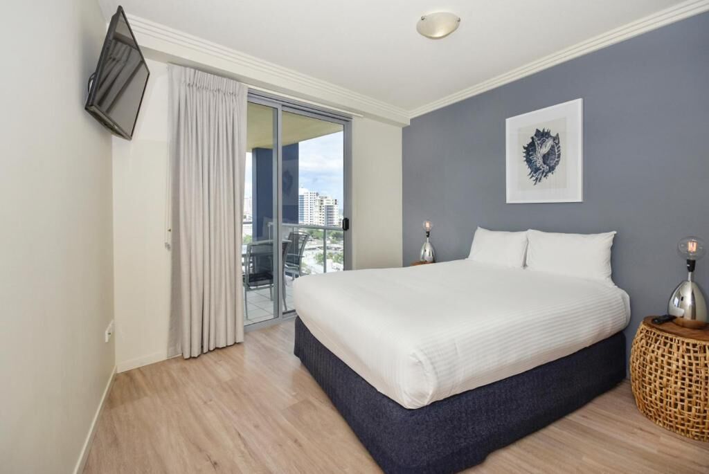 A bedroom with a large bed, a view of the city, a flat-screen TV, and a decorative wall piece.