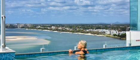 A person in a pool with a view of a beach and buildings in the distance.