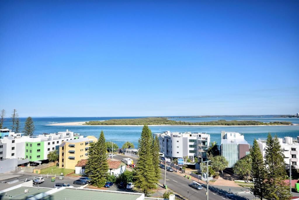 A coastal urban area with modern buildings, a clear blue sky, and a beach in the background.