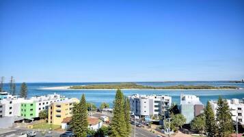 A coastal urban area with modern buildings, a clear blue sky, and a beach in the background.