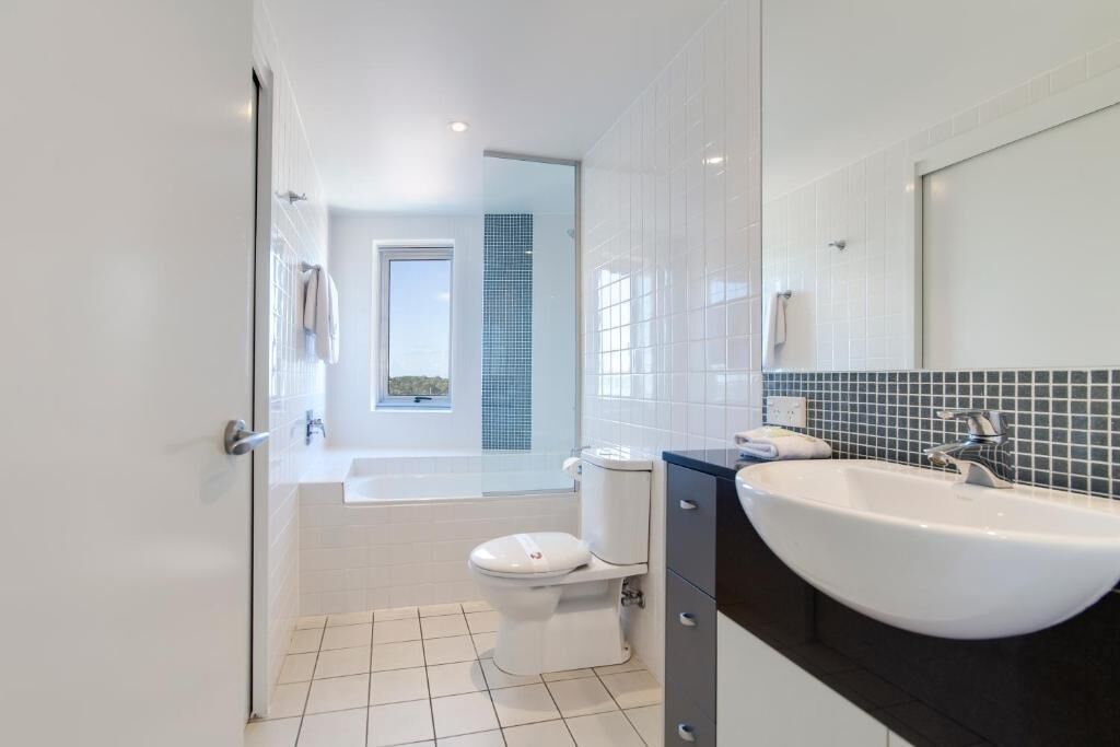 Une salle de bain moderne avec des toilettes blanches, un grand lavabo et un miroir.