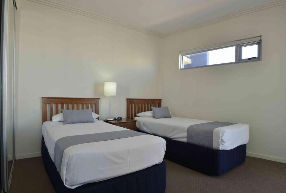 A hotel room with two beds, a nightstand, a lamp, and a window.