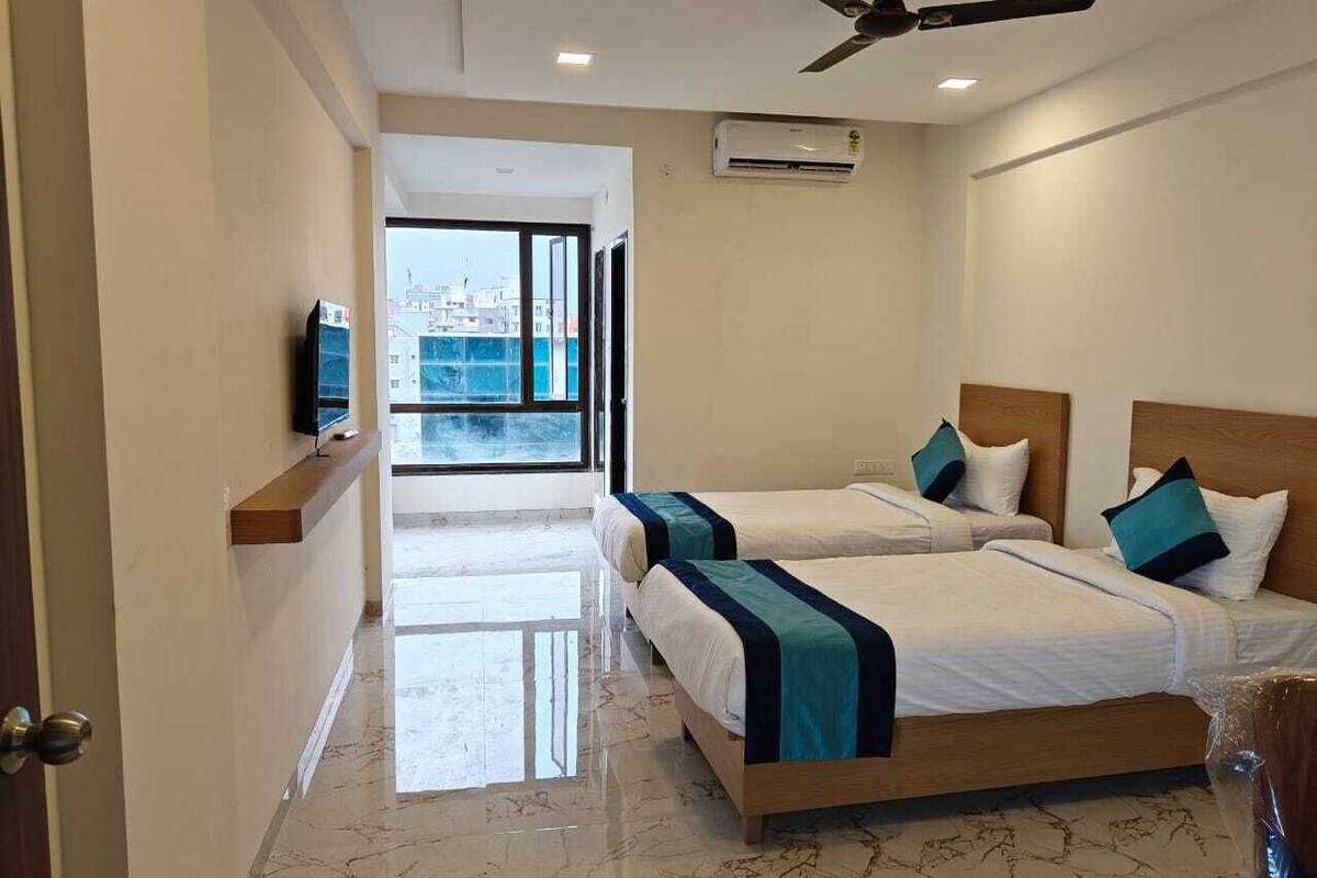 A hotel room with two beds, a ceiling fan, an air conditioning unit, and a television on a shelf.