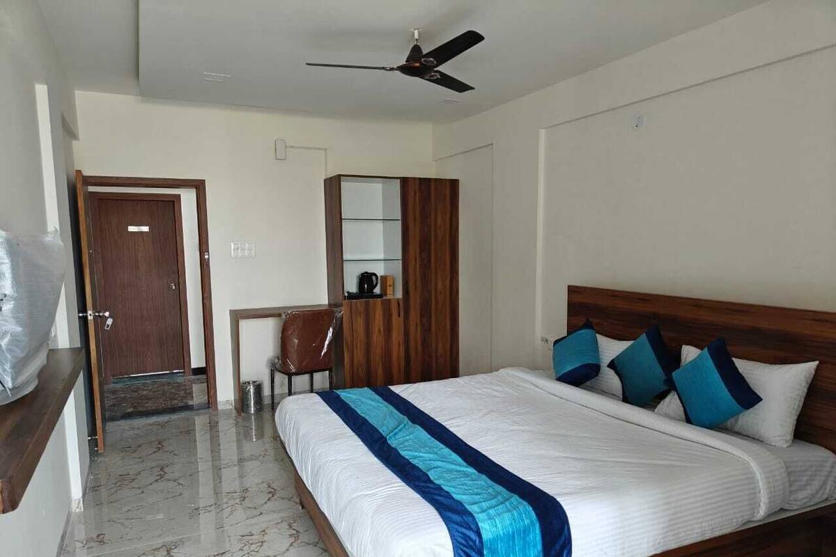 A bedroom with a bed, a ceiling fan, a wooden wardrobe, a desk, and a chair.