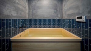 Una bañera rectangular con base de madera, frente a una pared con mosaicos azules.