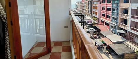 A balcony with a checkered floor, a wooden railing, and a view of a street with buildings.