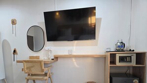A modern room with a mounted TV, a desk with a chair, a small refrigerator, and a security safe. - Charm Hostel at Jomtien (Pattaya)