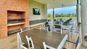 Une terrasse extérieure avec une cheminée en briques, des chaises en métal blanc et une table en bois.