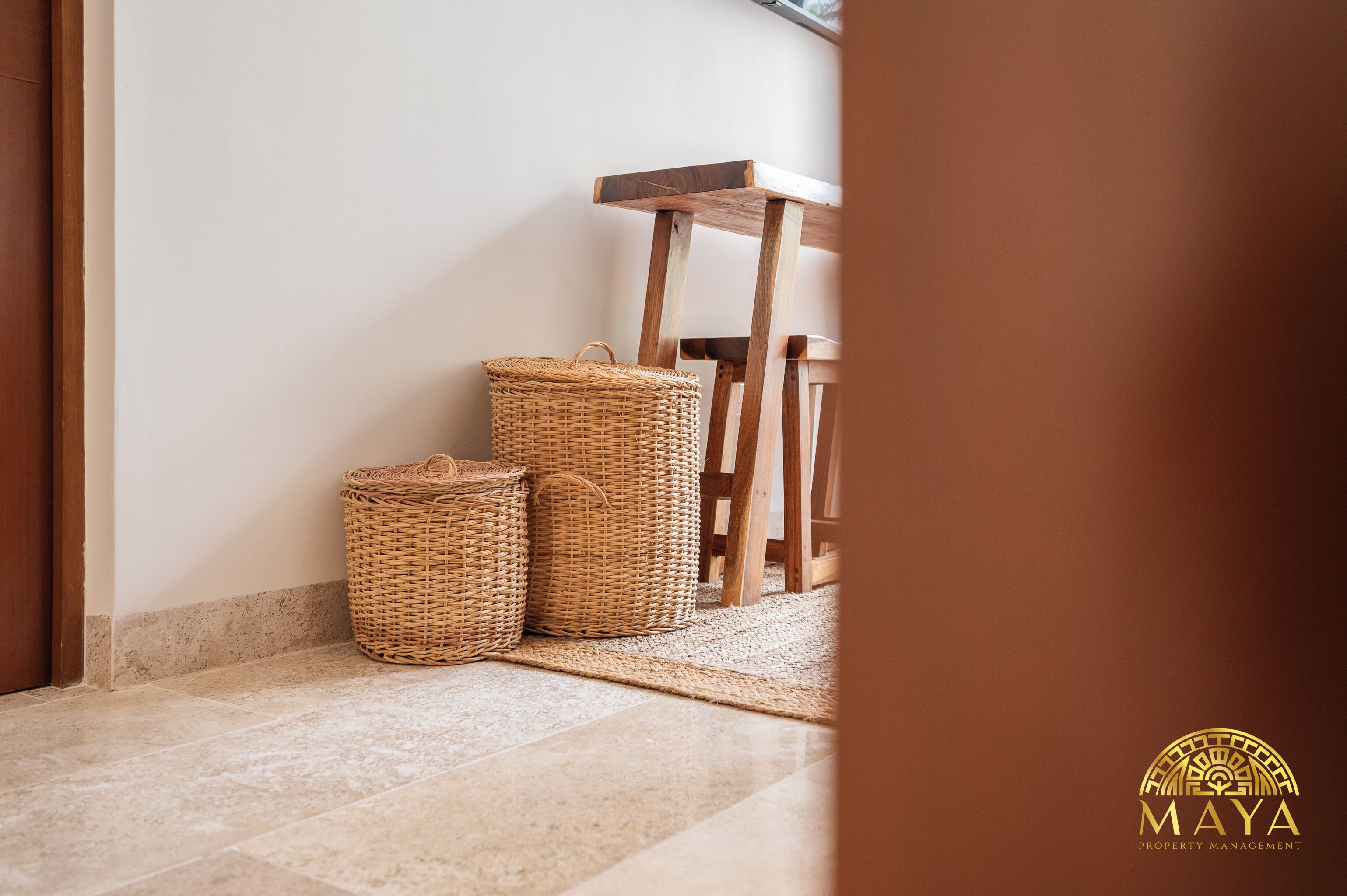 Rincón de una habitación con una silla de madera y dos cestas de mimbre sobre un suelo de baldosas.