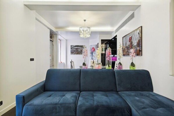 A living room with a blue sofa, a chandelier, and artwork on the walls.