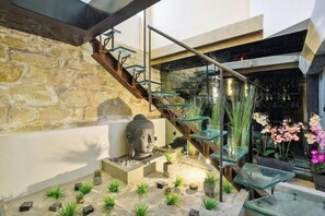 Una escalera moderna con barandillas de vidrio, una pared de piedra y una estatua de Buda.