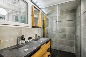 Un baño con lavamanos doble, un espejo, ducha y pared con azulejos.