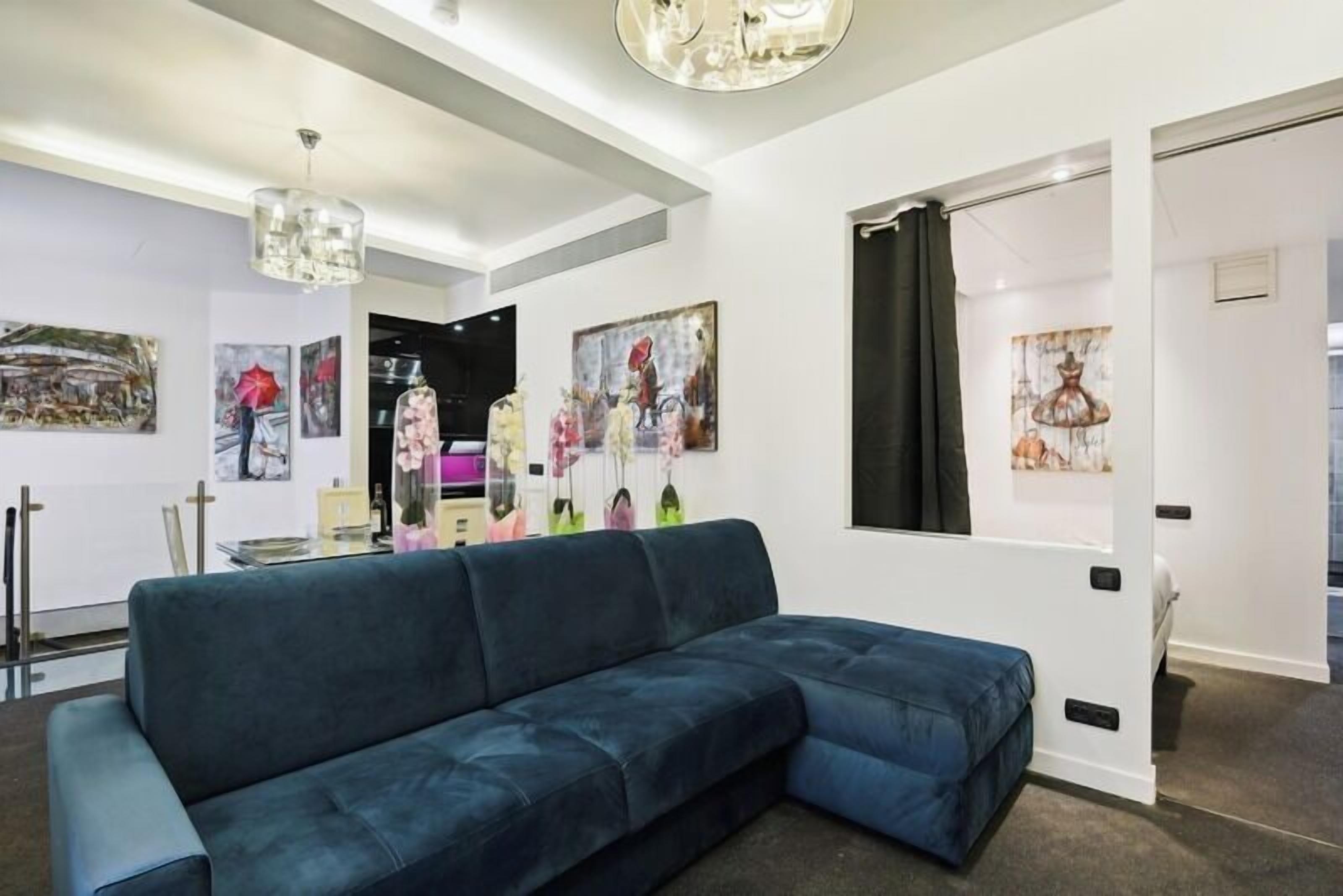 A modern living room with a sectional sofa, artwork on the walls, and a chandelier.