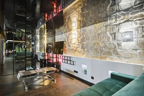 Un interior moderno con una pared de piedra, un sofá verde y una mesa con estructura metálica.