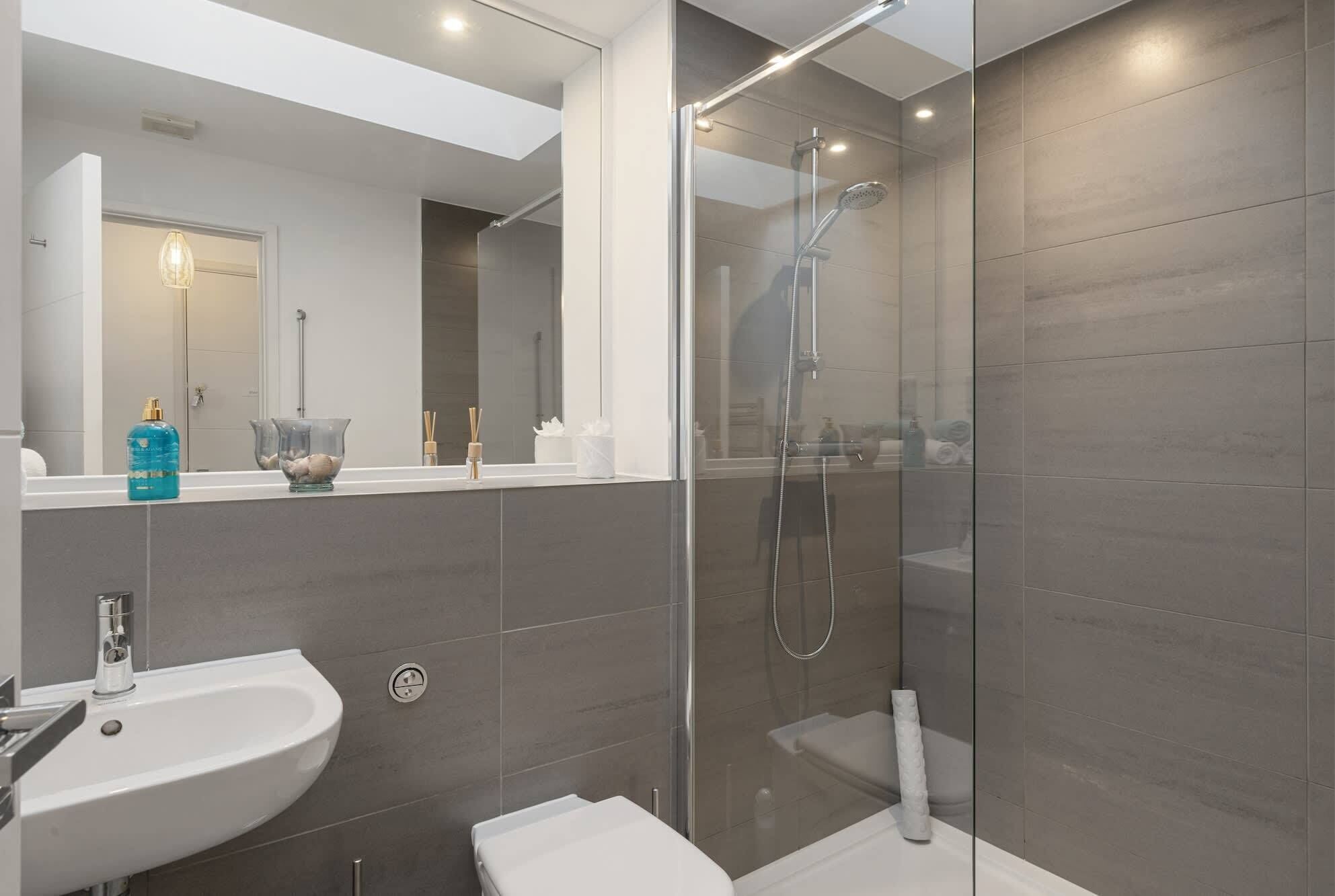 A modern bathroom with a glass-enclosed shower, a white sink, and a toilet.