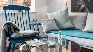 A modern living room with a blue chair, a sofa with white cushions, a glass coffee table with magazines, and decorative items. - Nice home in Rønne with WiFi (Rønne)