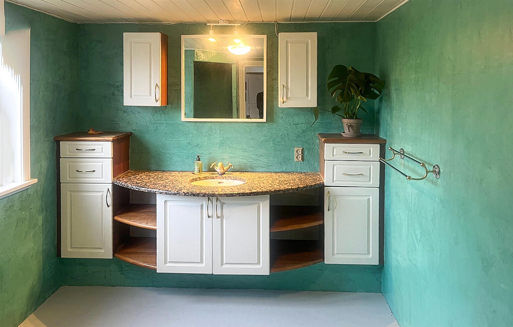Une salle de bain avec un mur vert, un lavabo doté d’un plan de travail en granit et des meubles blancs.