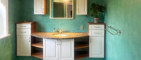 Une salle de bain avec un mur vert, un lavabo doté d’un plan de travail en granit et des meubles blancs.